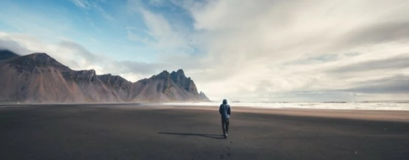 Heavn : Une personne debout sur une plage noire avec des montagnes en arrière-plan, parcourant l'application de rencontre chrétienne Heavn.